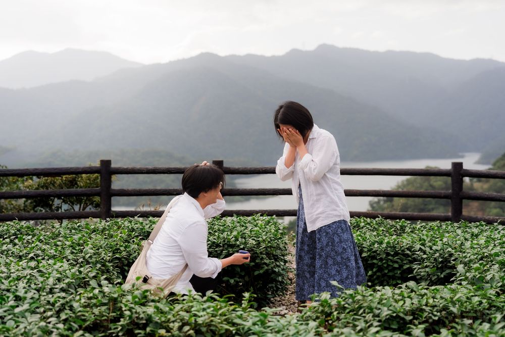 People sitting on a wooden fence overlooking a scenic mountain landscape with green tea fields below.