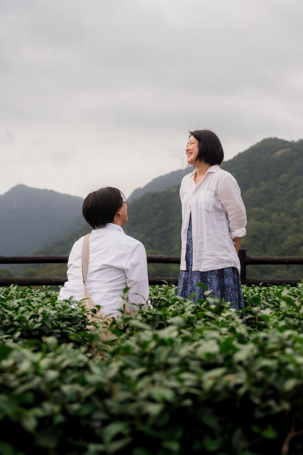 Two people share a joyful moment together in a lush mountain landscape with green tea fields.
