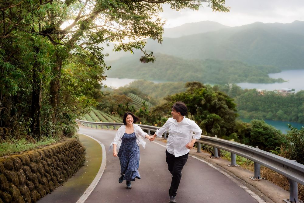 Two people walk together on a scenic mountain path surrounded by lush greenery and scenic views.