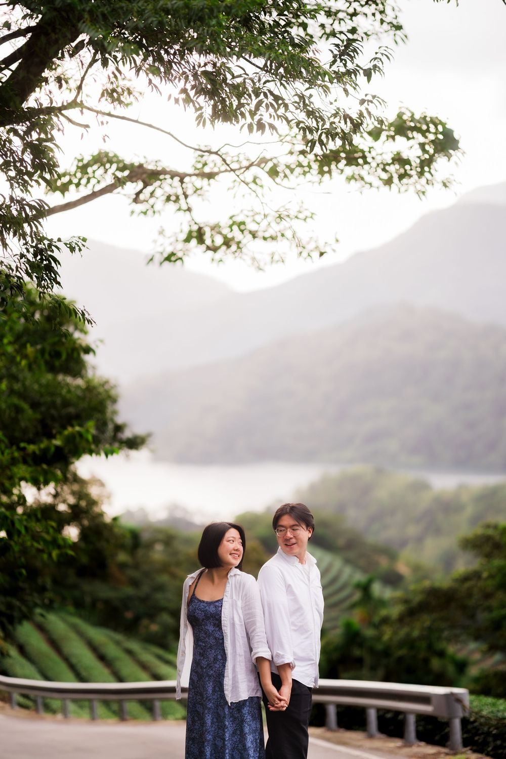 Couple enjoying a romantic moment on a scenic overlook with misty mountains and lush greenery in the background.
