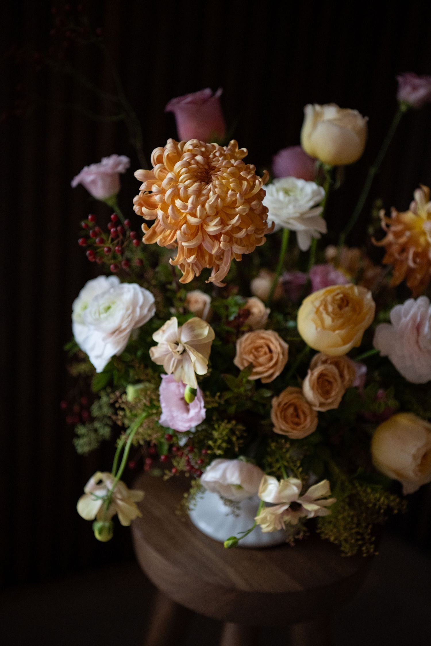 Moody floral arrangement with peach and cream roses in dark lighting creating dramatic shadows.