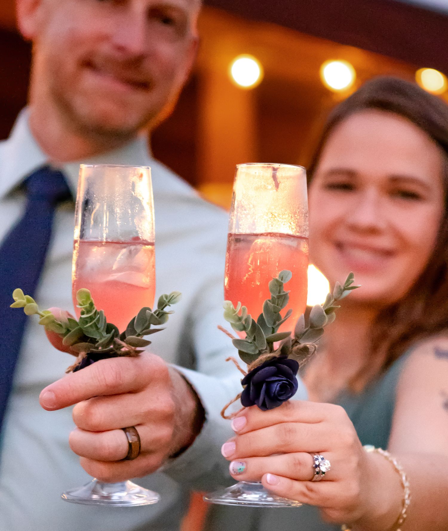 Candlelit glasses decorated with greenery being held in celebration.