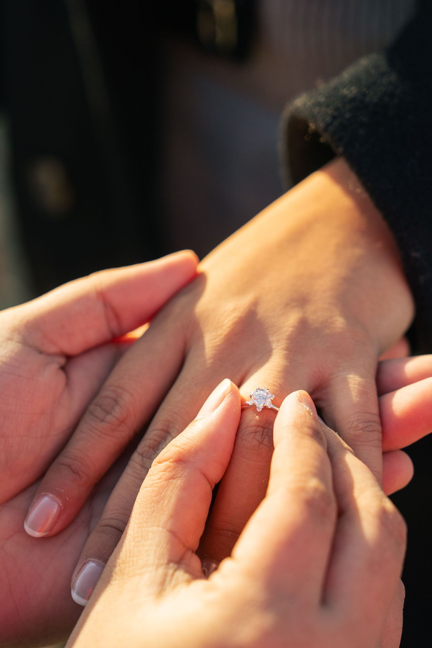 A close-up shot of hands placing an engagement ring with a sparkling diamond on a finger in warm lighting.