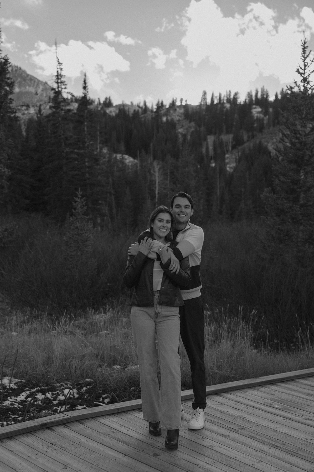 A couple dances together on a wooden deck surrounded by mountain scenery and evergreen trees.