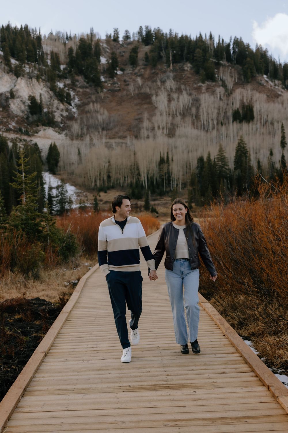 Two people walk and play together on a wooden boardwalk surrounded by autumn mountain scenery.