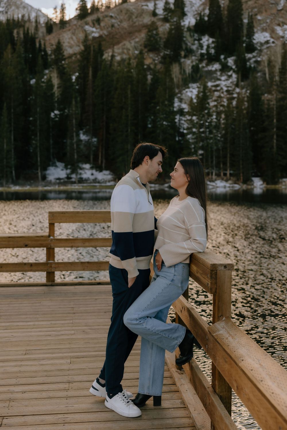 A couple shares a tender moment while sitting on a wooden bench in a scenic mountain landscape at sunset.