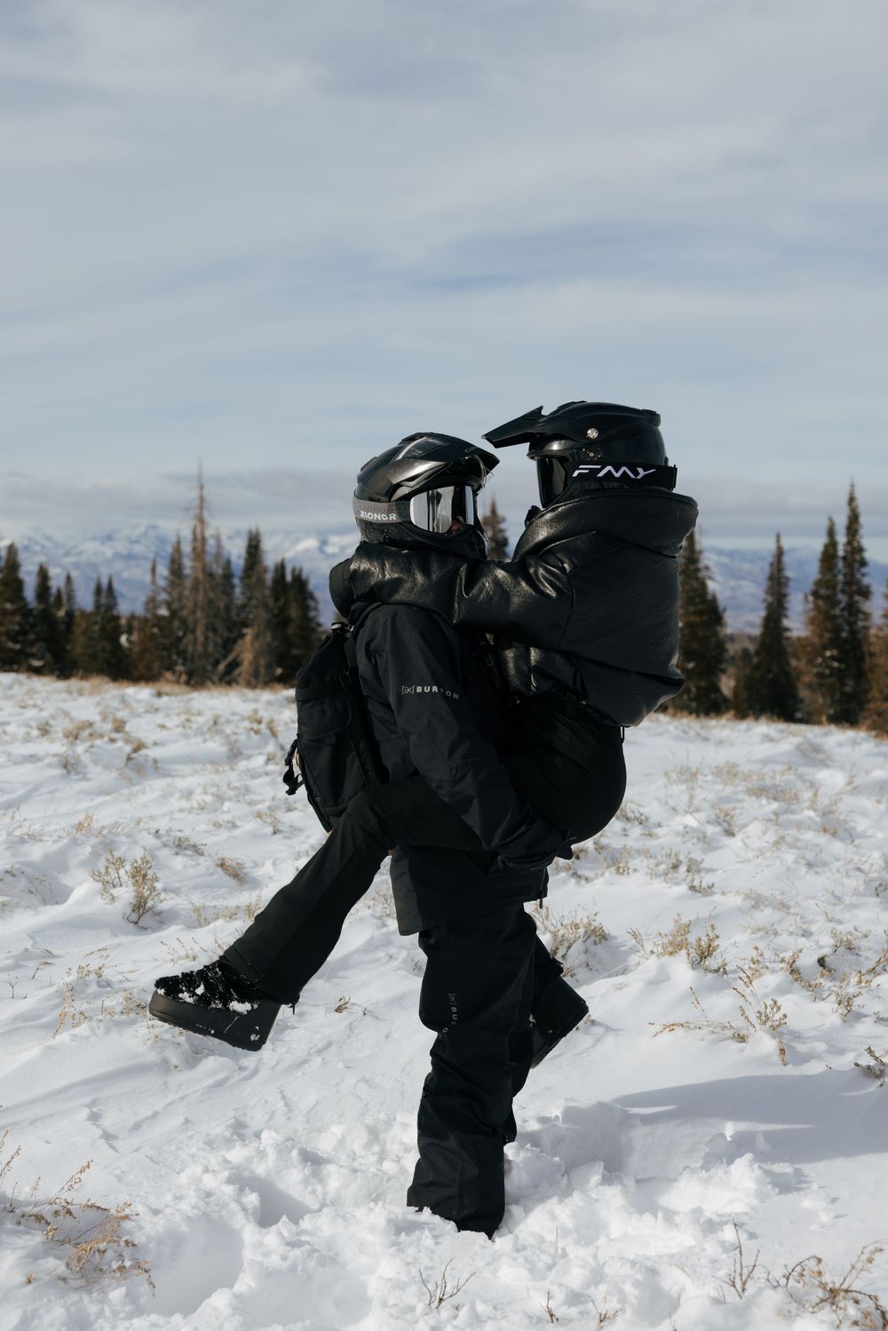 A sequence of black backpacks falling into deep snow against a winter mountain landscape with evergreen trees.