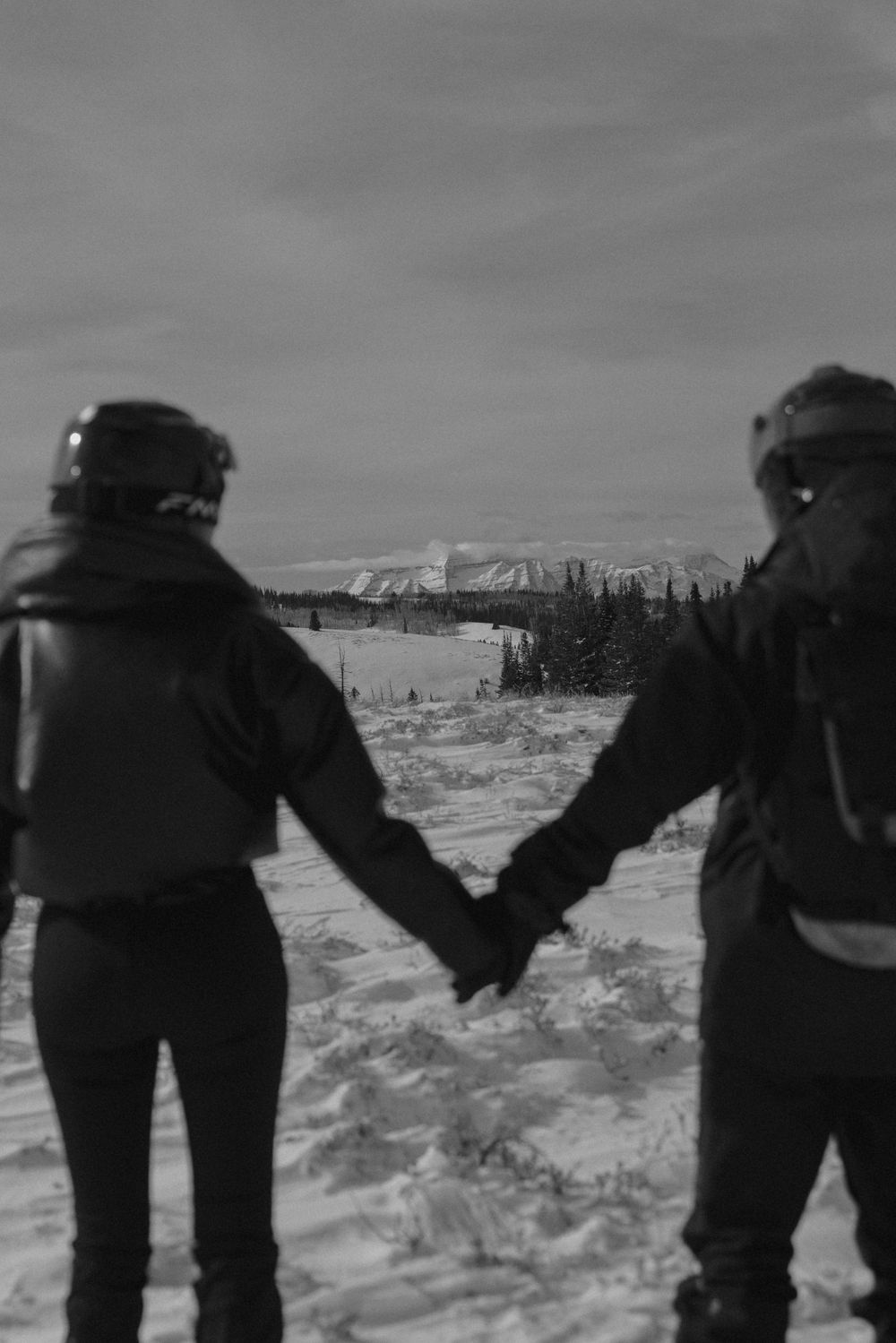 A group of people hold hands in a line while walking through a snowy winter landscape.