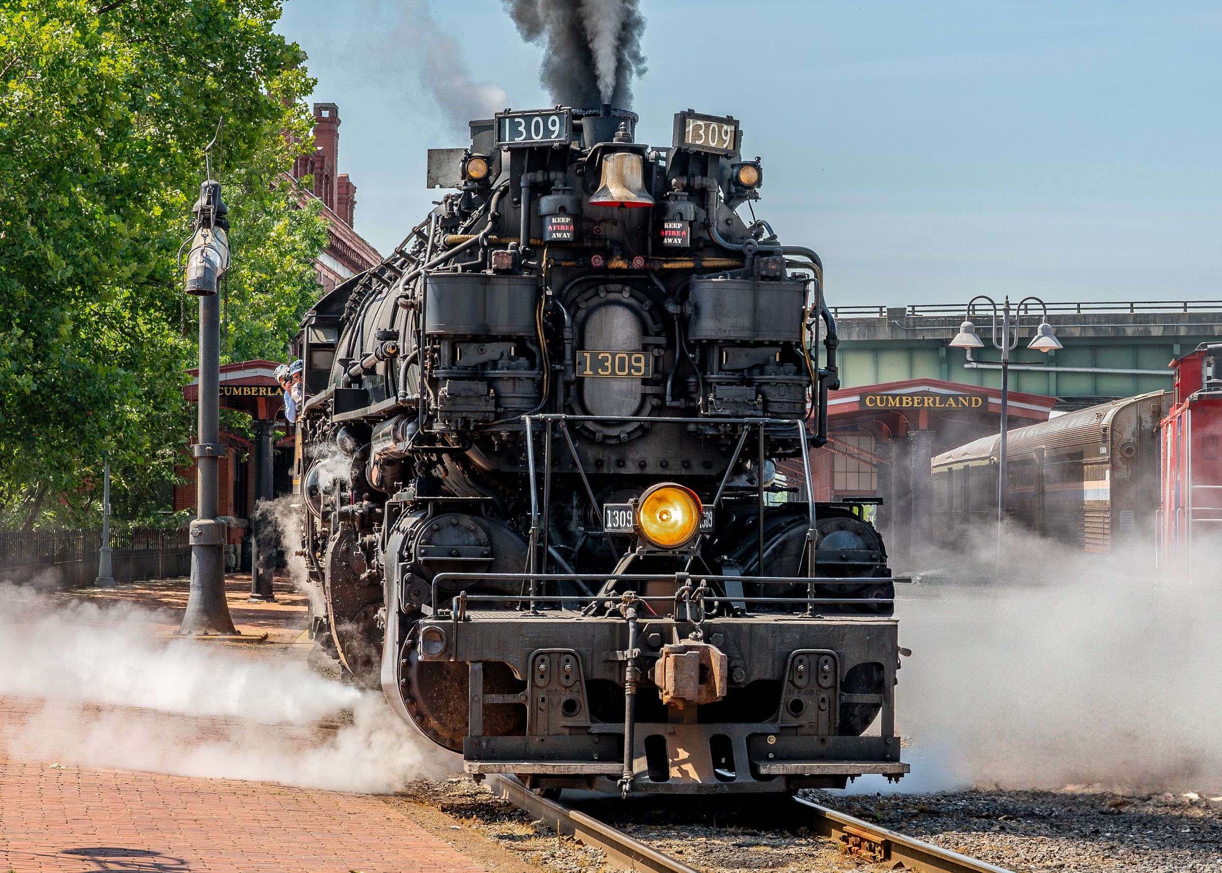 A vintage steam locomotive releases clouds of white steam while stationed at a railway platform.