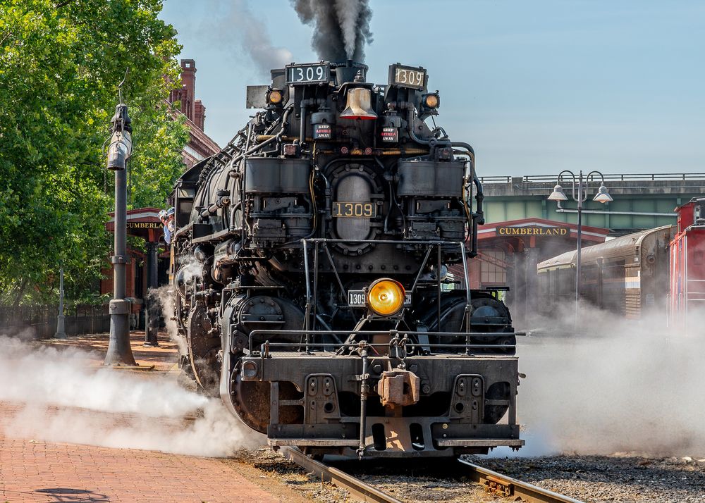A vintage steam locomotive releases clouds of white steam while stationed at a railway platform.
