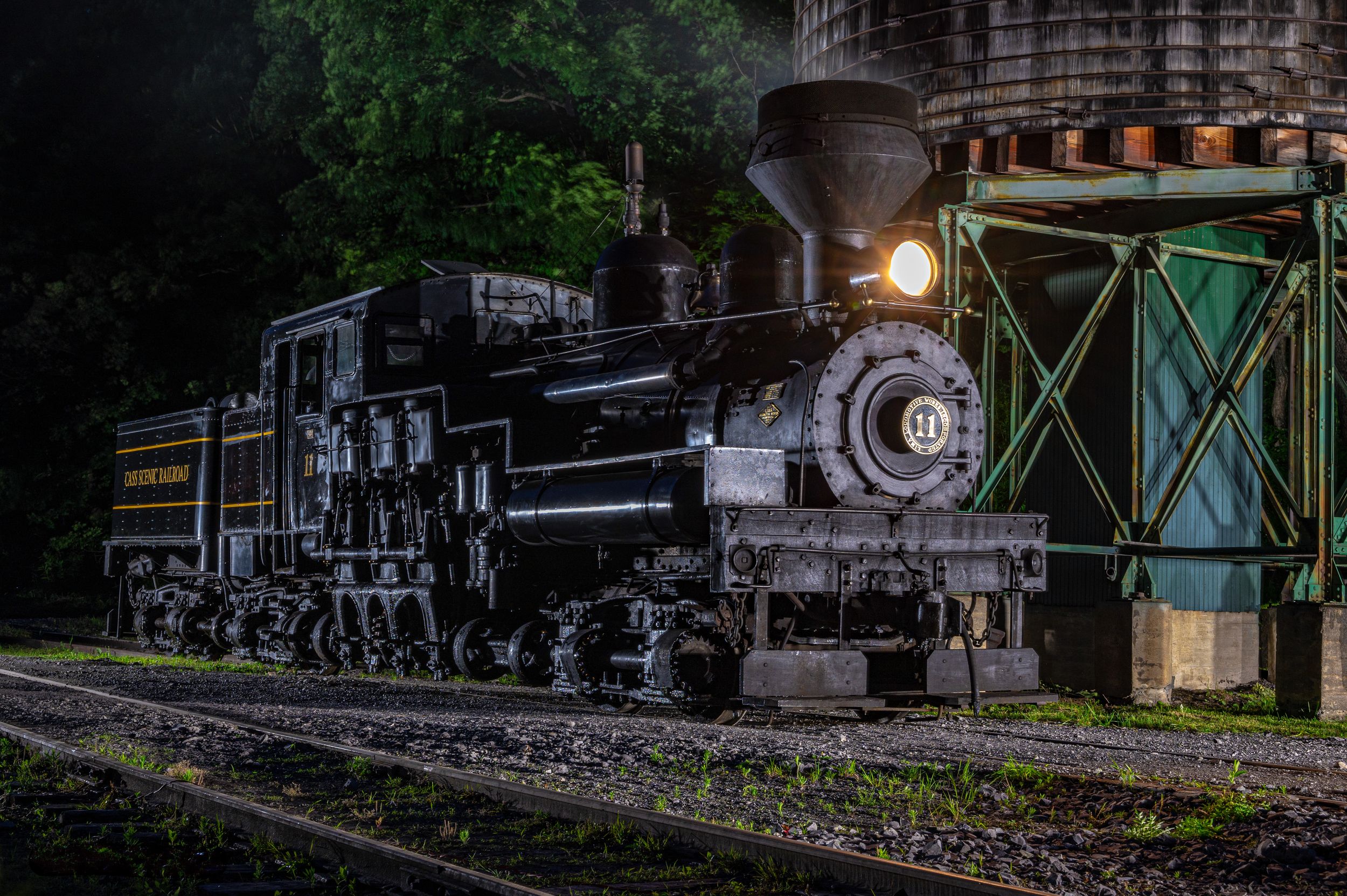 Vintage steam locomotives and train cars displayed in an outdoor railroad museum at dusk.
