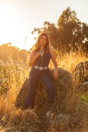 Person in western-style denim poses on hilltop during golden hour.