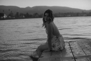 Black and white portrait of person sitting on lakeside dock at dusk.