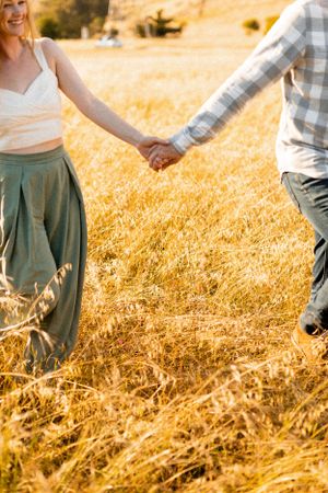 Couple holding hands while walking through tall golden grass at sunset.