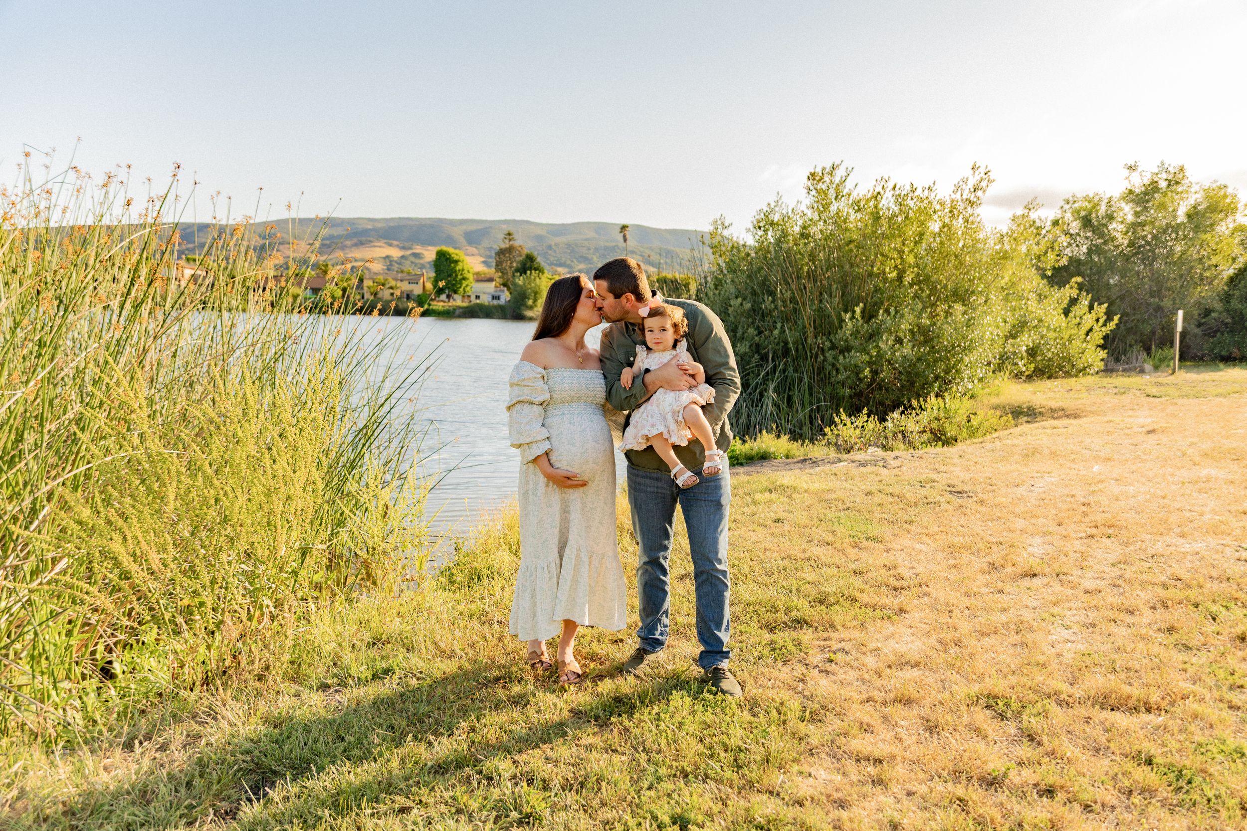 A romantic sunset engagement photoshoot at a scenic overlook with golden grass and sunlit mountains in the background.