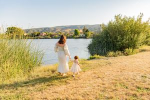 A mother and child stroll through a scenic grassy path along the waterfront on a sunny summer day.