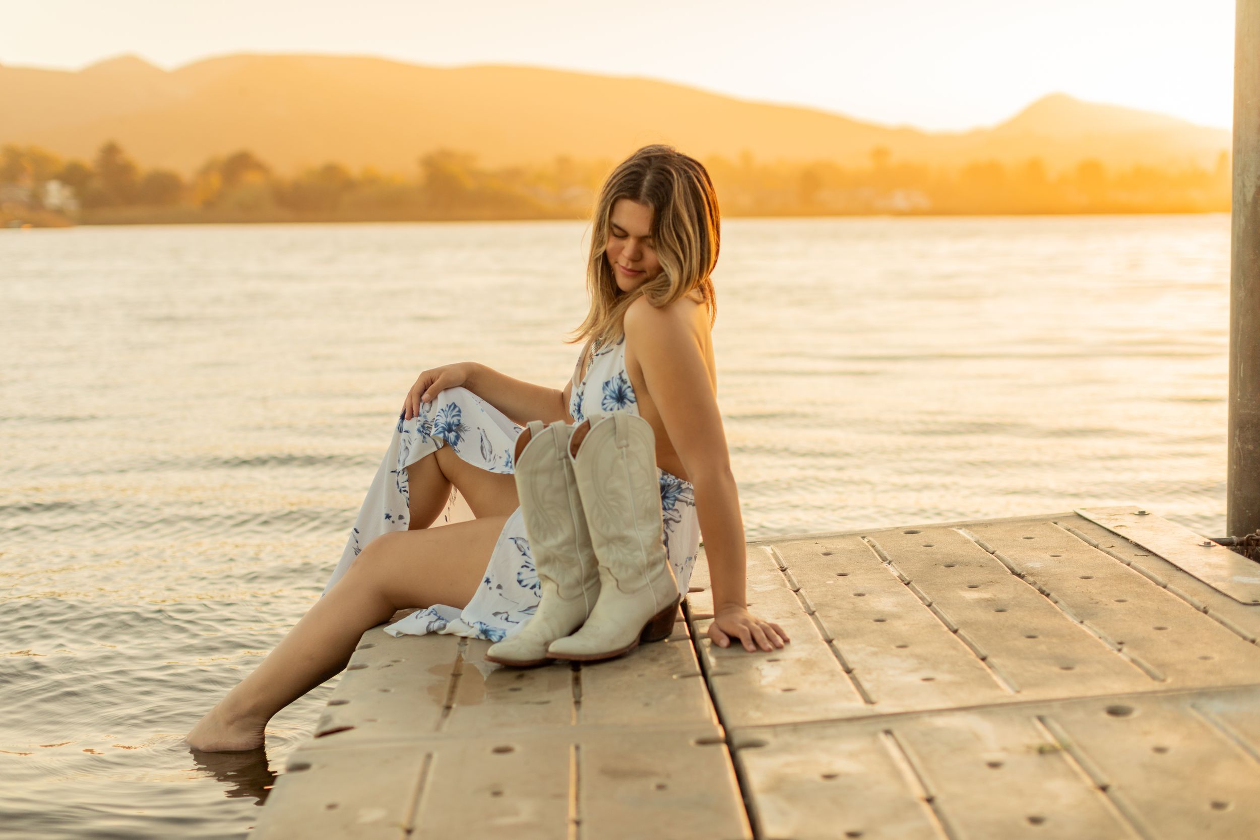 Person in floral dress poses on wooden pier during warm sunset.