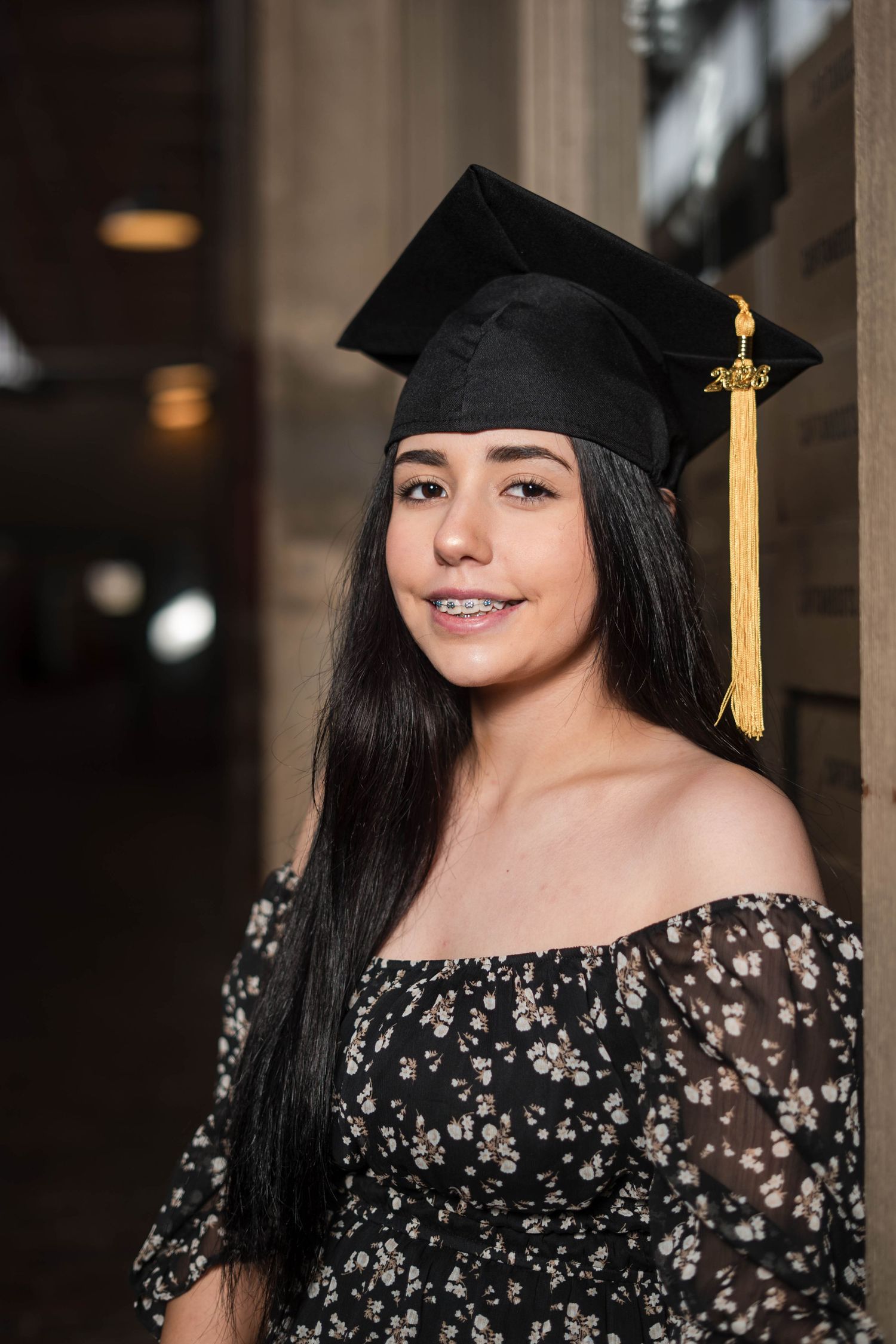 Young woman wearing a black graduation cap with gold tassel and floral off-shoulder dress.