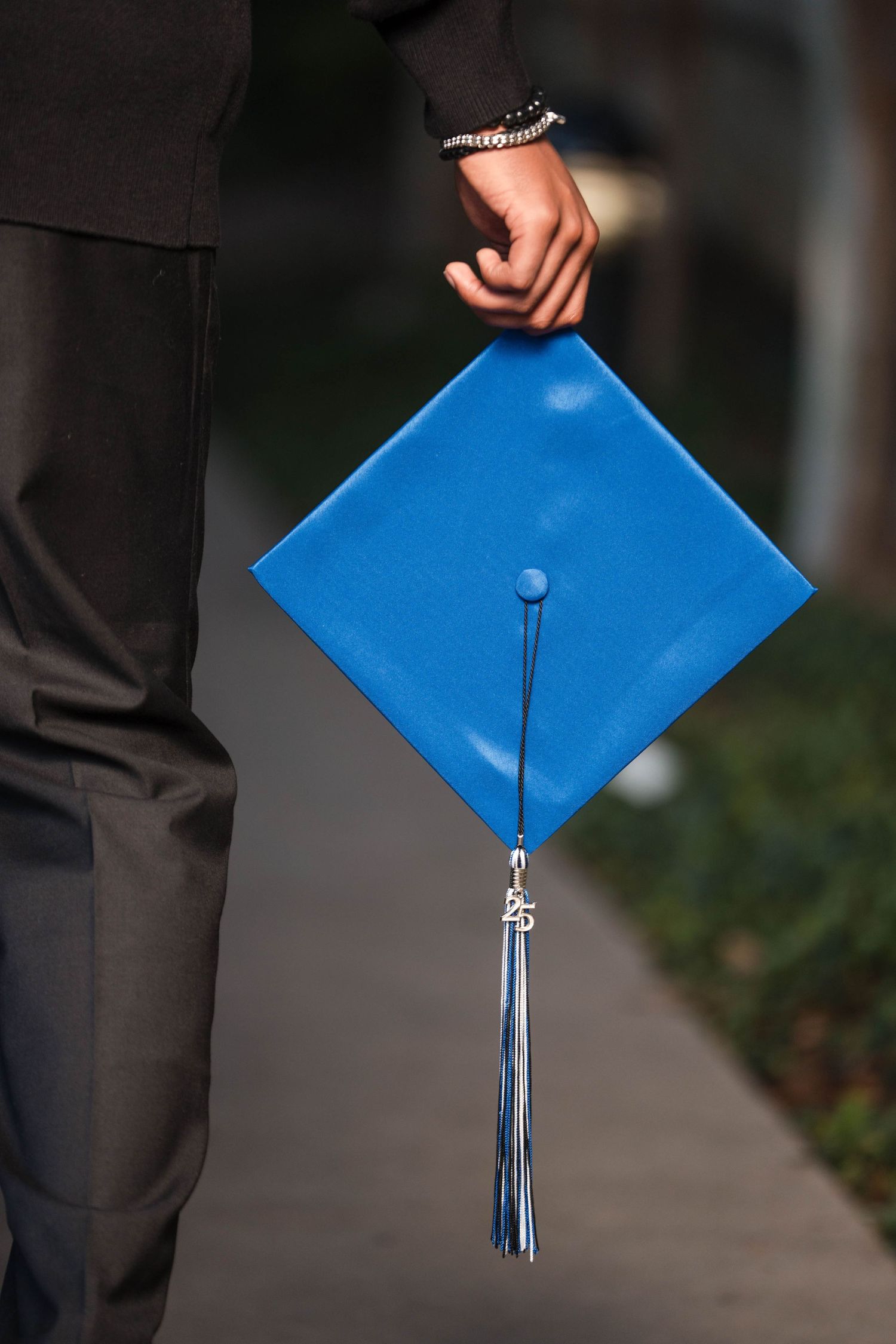 Graduate holds blue mortarboard cap with tassel while wearing black graduation gown.