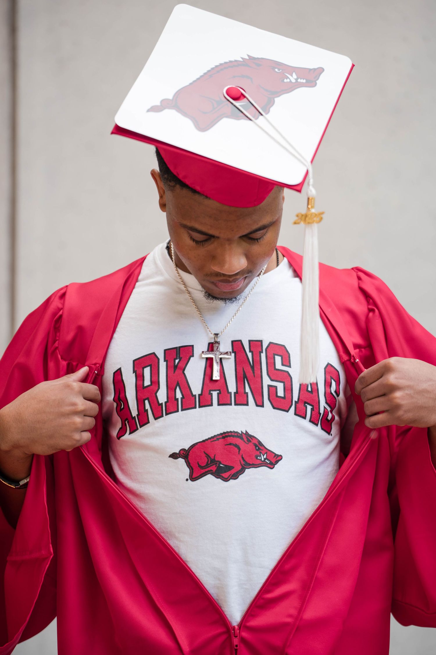Young man in red Arkansas graduation cap and gown revealing Arkansas t-shirt underneath.