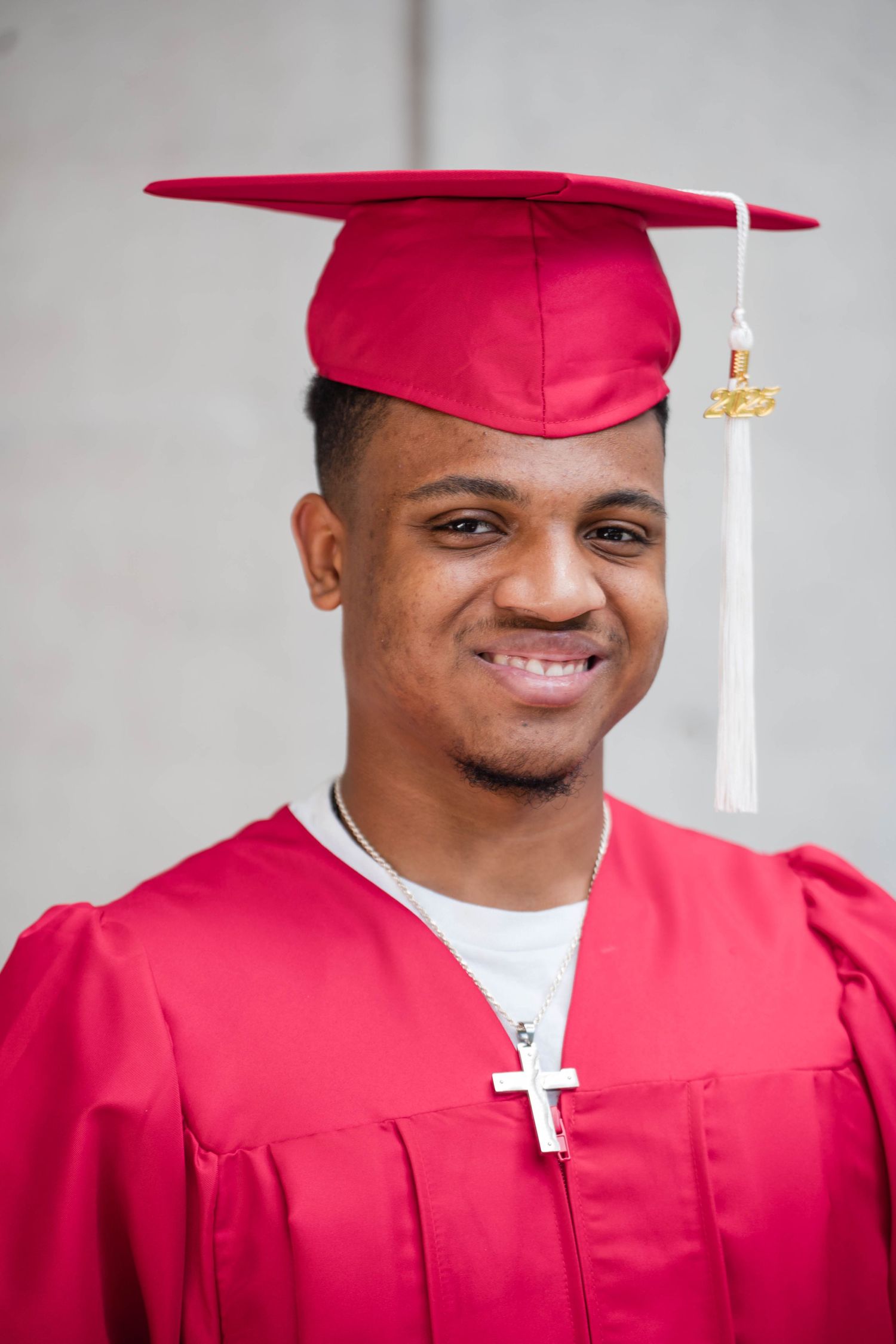 Close-up portrait of smiling graduate in red cap and gown with cross necklace.