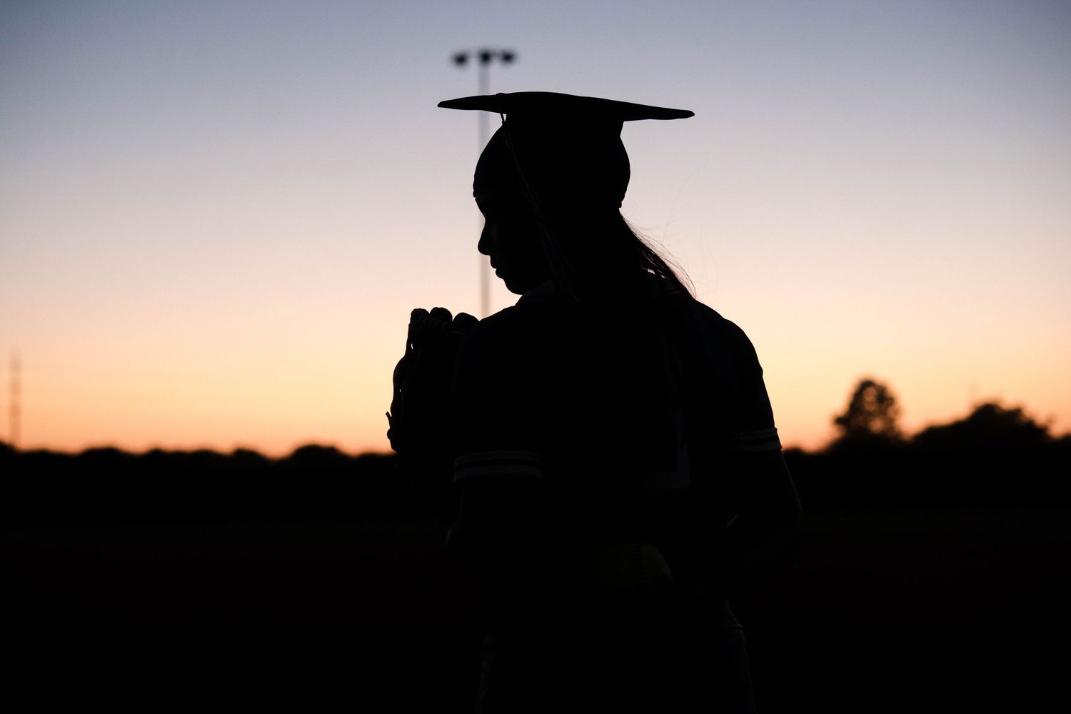Silhouette of female graduate in cap and gown against colorful sunset sky.