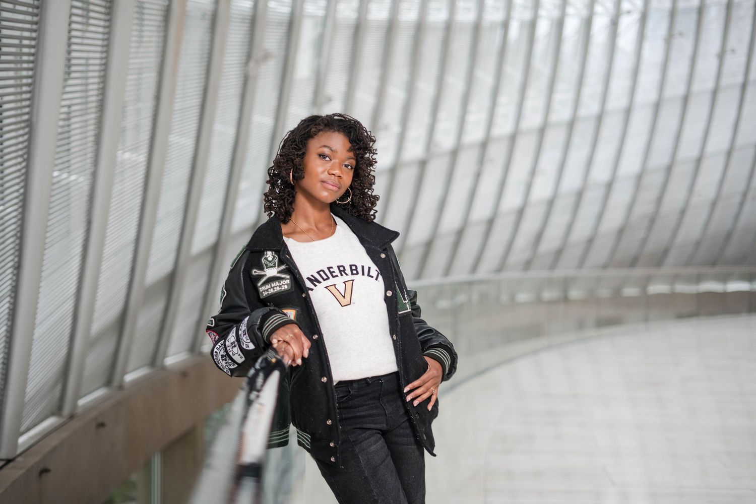 Young woman in Vanderbilt varsity jacket poses confidently in modern architectural space with metal railings.