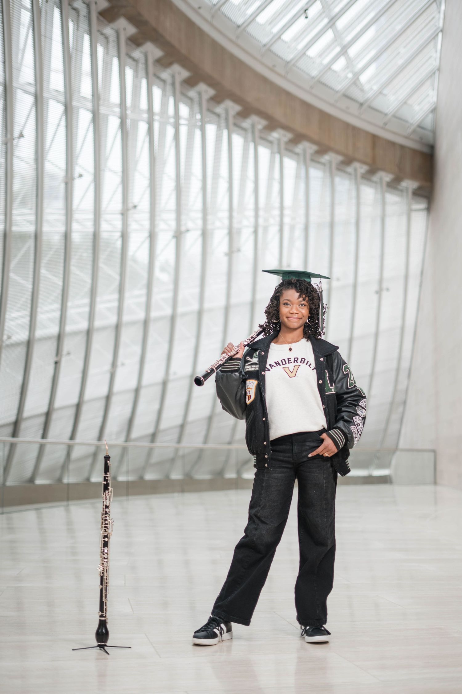 Graduate in cap and Vanderbilt shirt holds clarinet in modern architectural space.