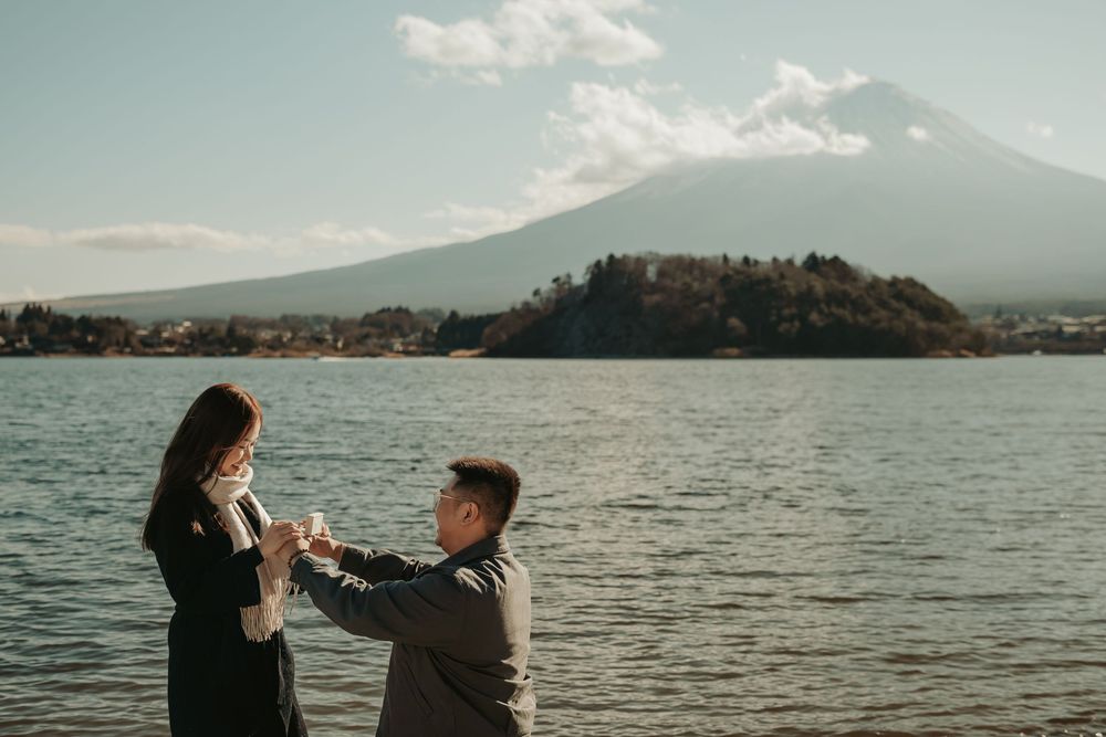 Couple embracing by a serene mountain lake during sunset, with scenic views of the landscape in the background.