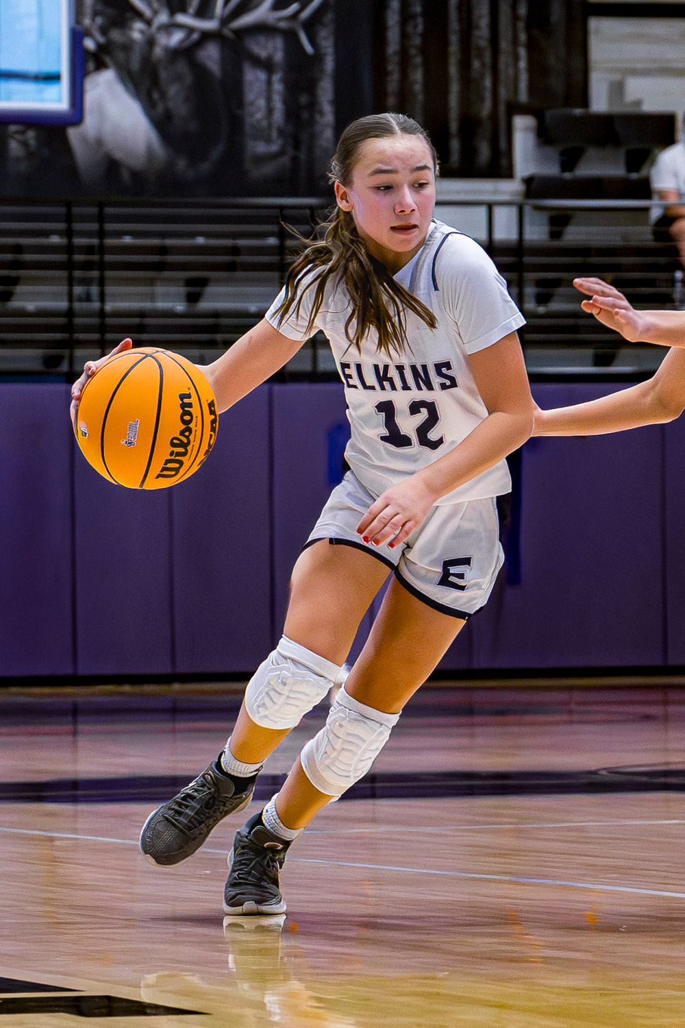 Elkins JV Basketball player in white jersey dribbles the ball during intense game action on indoor court.