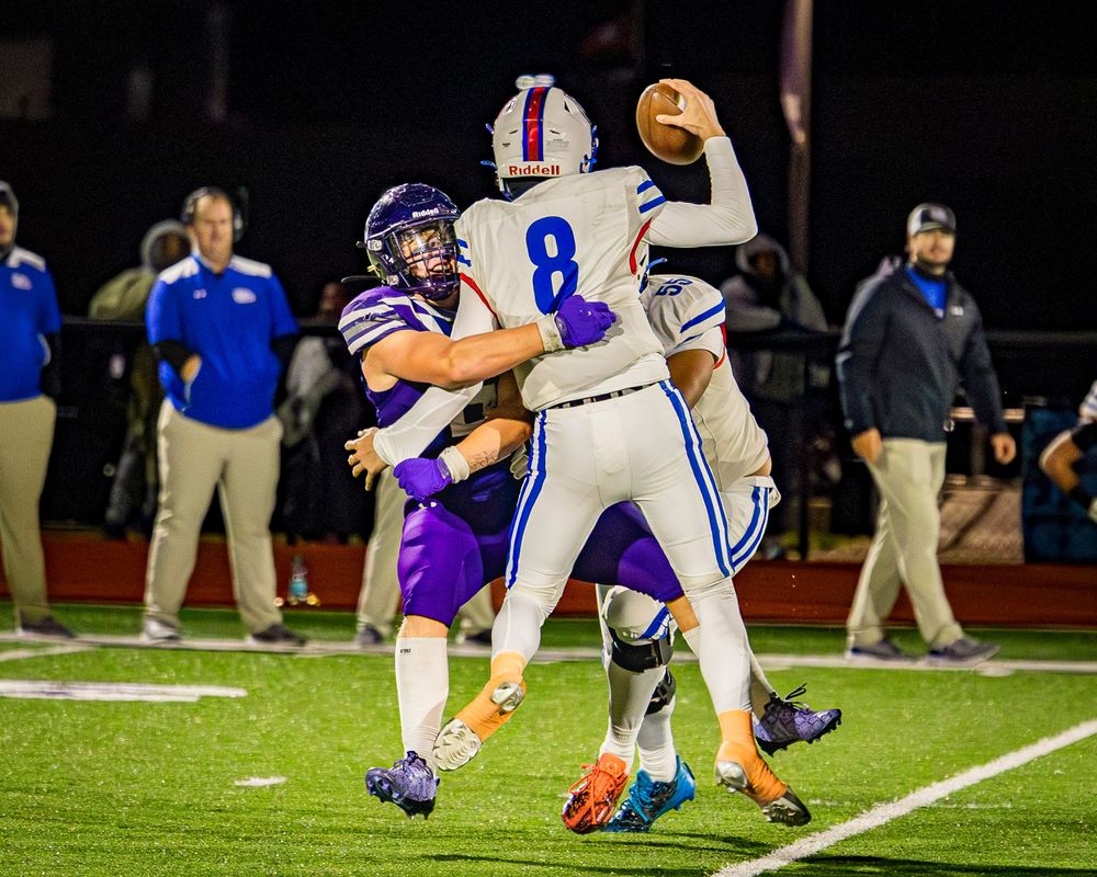 Elkins Arkansas High school football defensive player Cason Roten tackles quarterback during night game on artificial turf field.