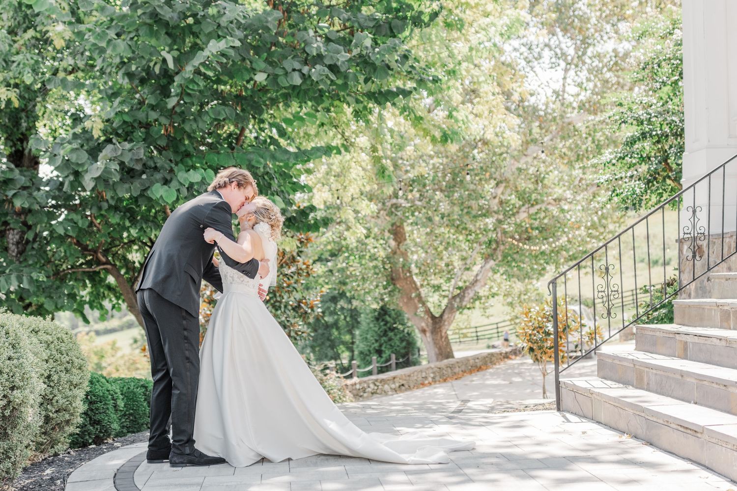 Bride's dramatic cathedral train trails behind couple on garden walkway during wedding portraits.