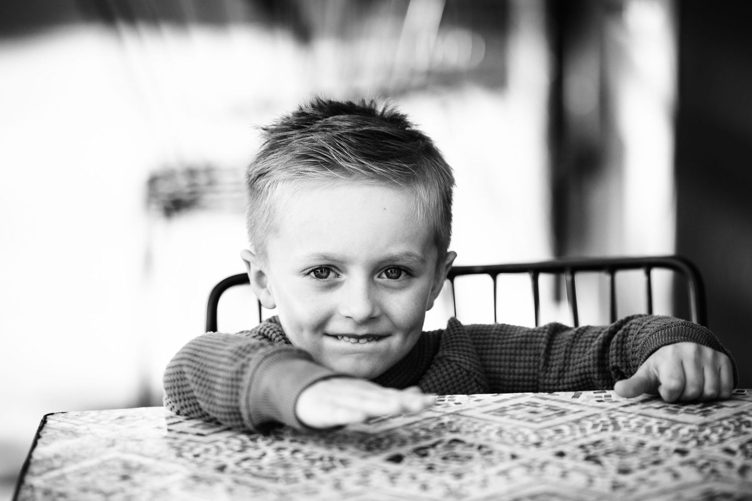 Black and white portrait of a smiling young boy leaning on a table with arms outstretched.