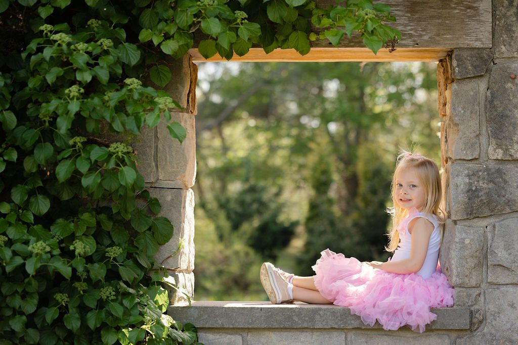 A series of outdoor portraits showing a young child in a pink tutu dress posing by a stone archway in a garden setting.