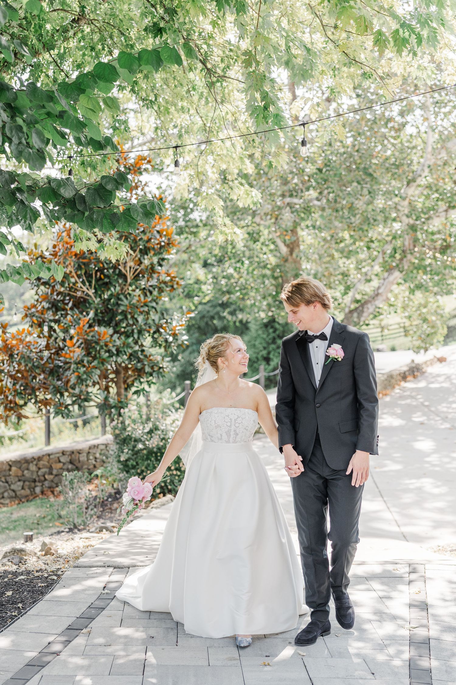 Wedding couple walking together on a stone pathway surrounded by lush greenery.