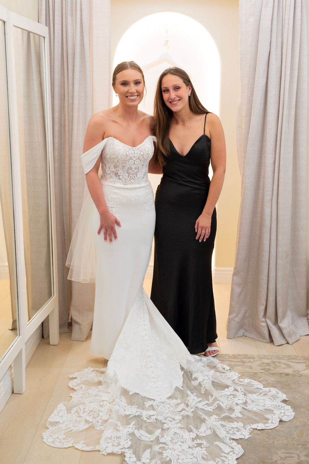 Wedding dress with intricate lace train displayed in elegant dressing room setting.