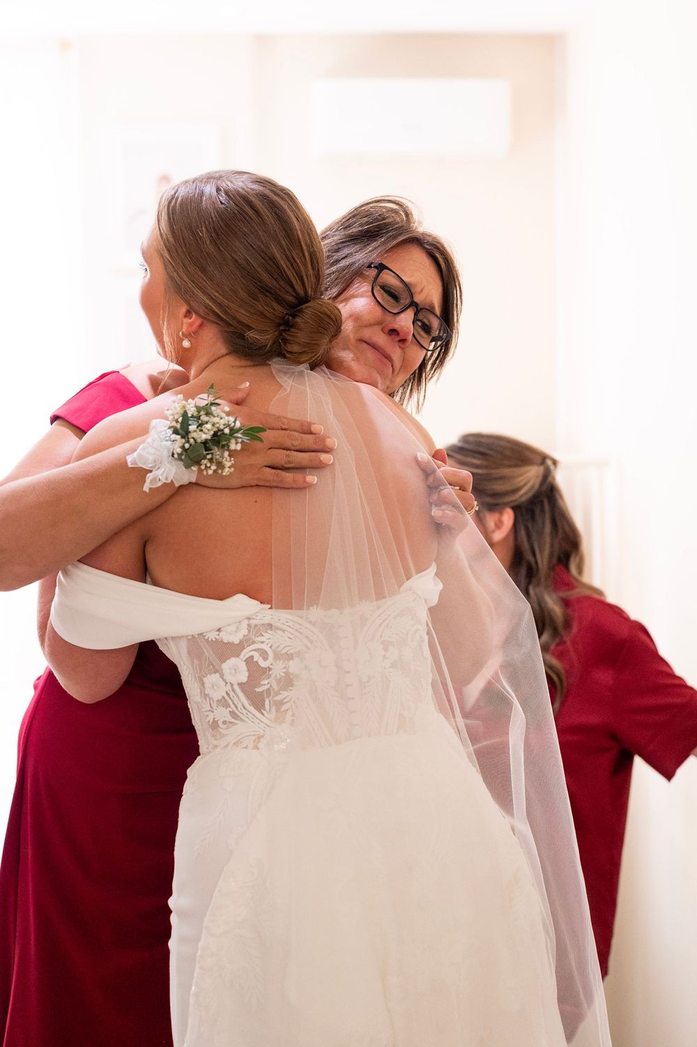 An emotional embrace between wedding attendees wearing red and white dresses with a corsage visible.