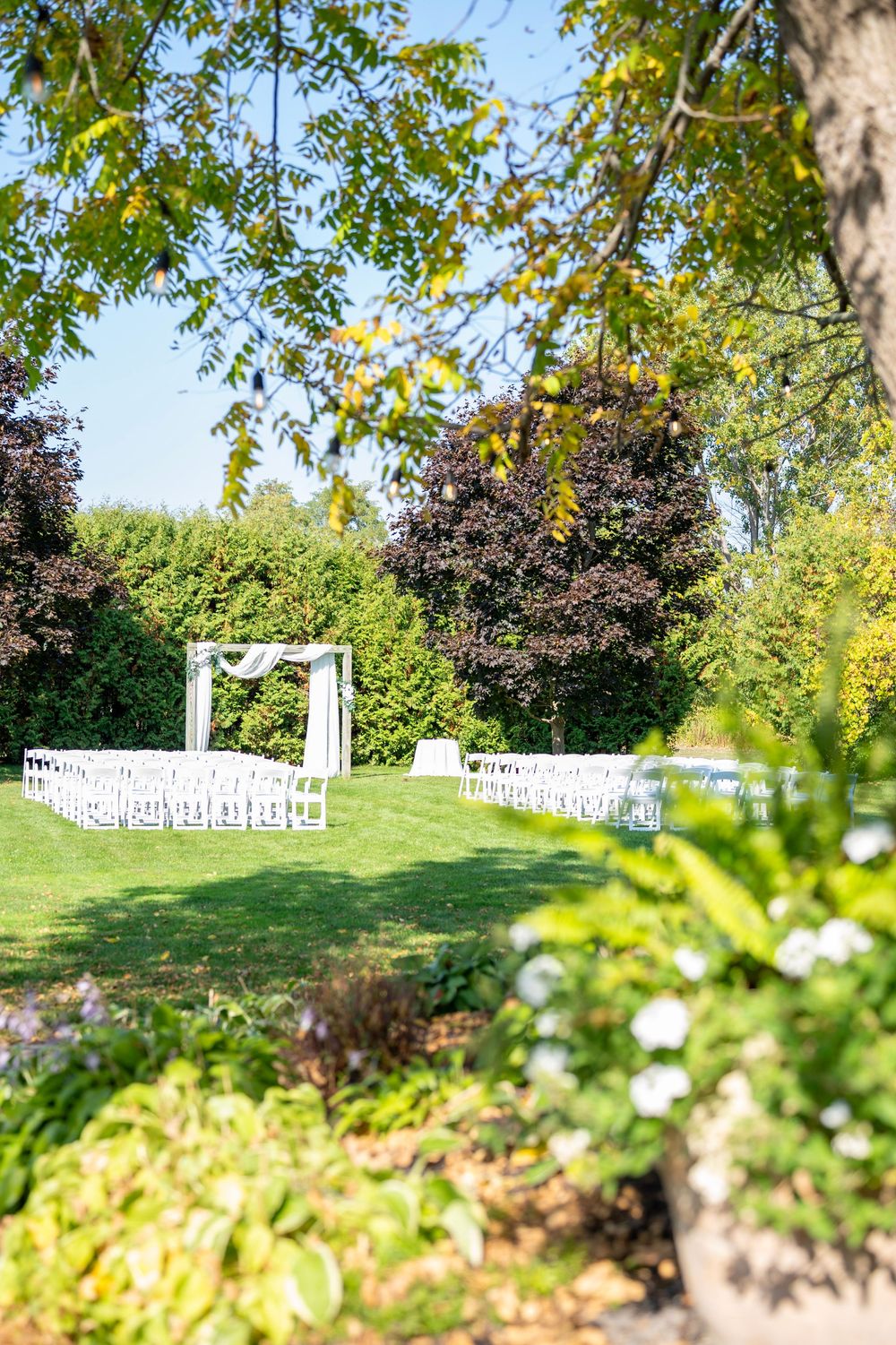 White wedding arch and chairs set up on manicured lawn surrounded by lush garden landscaping.