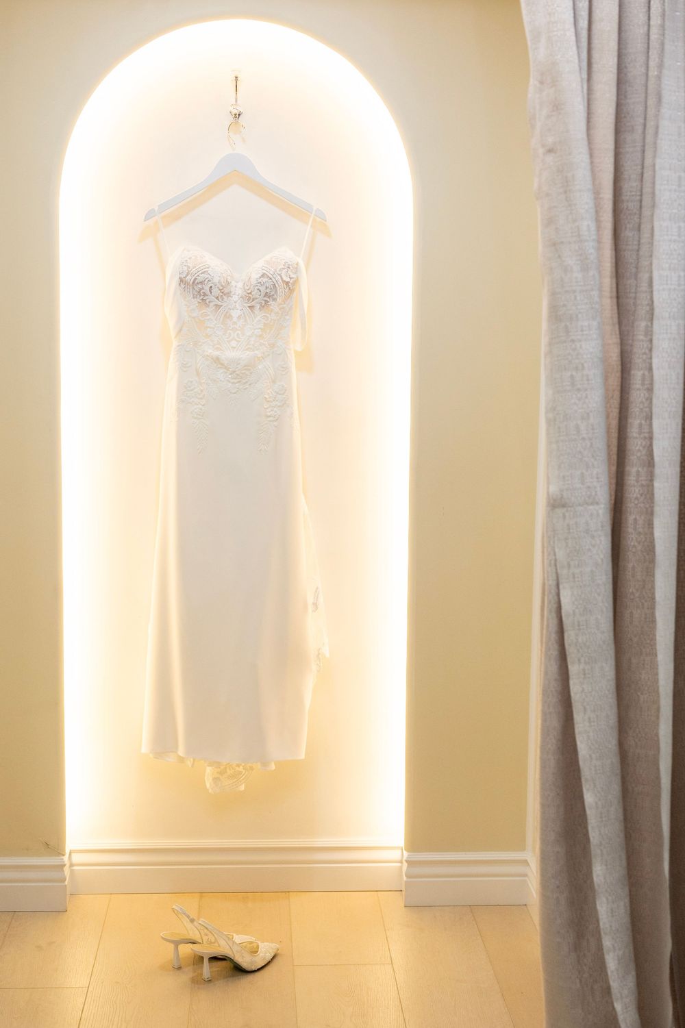 Illuminated wall niches display white wedding dresses against soft beige walls with gray curtains.