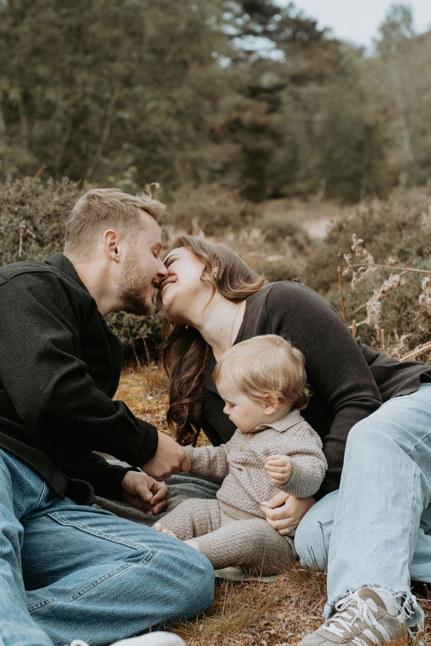 A couple shares an intimate moment in a field, with the person wearing a rust-colored sweater.