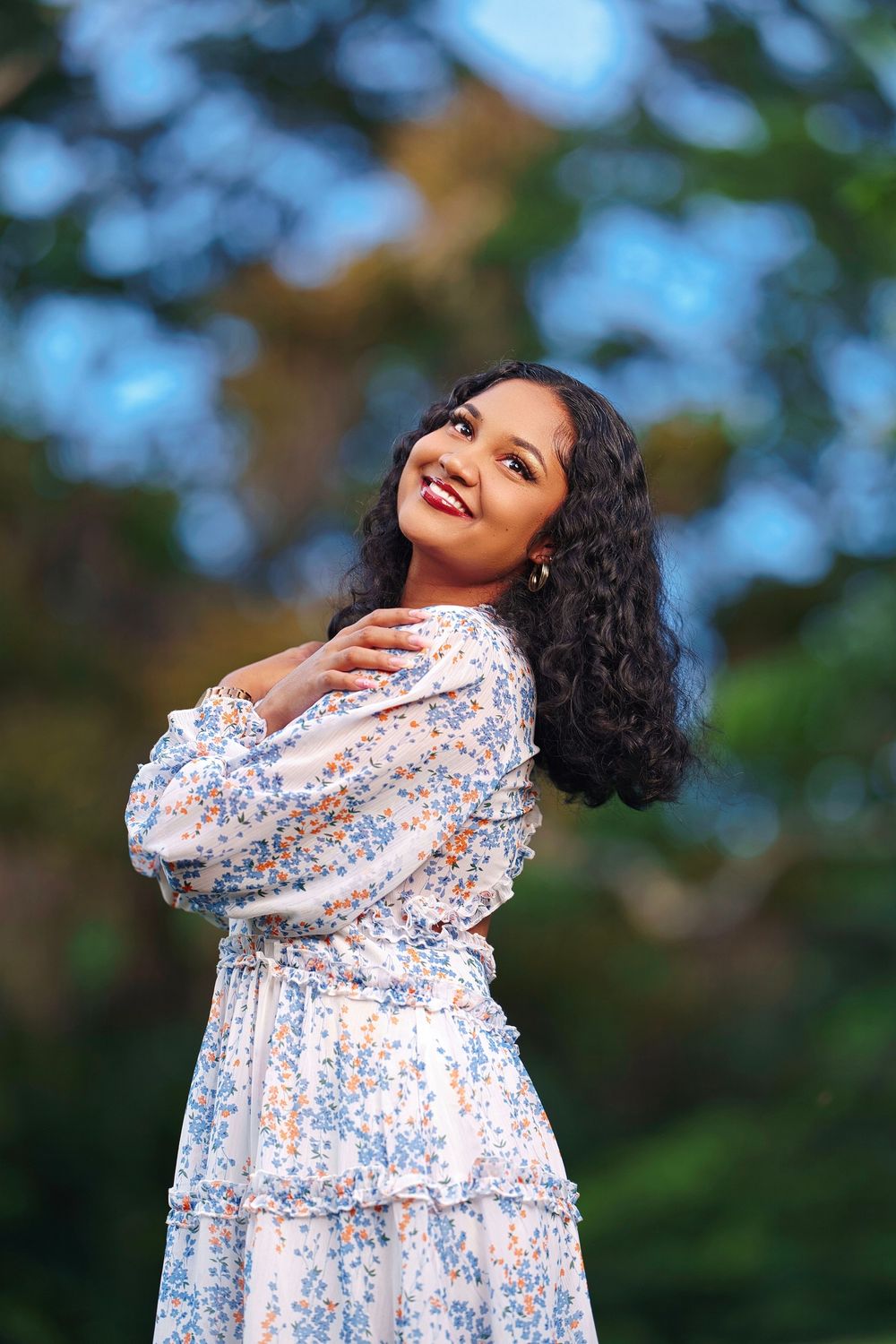 A woman in a floral dress poses joyfully against a blurred natural background in a sequence of outdoor portraits.