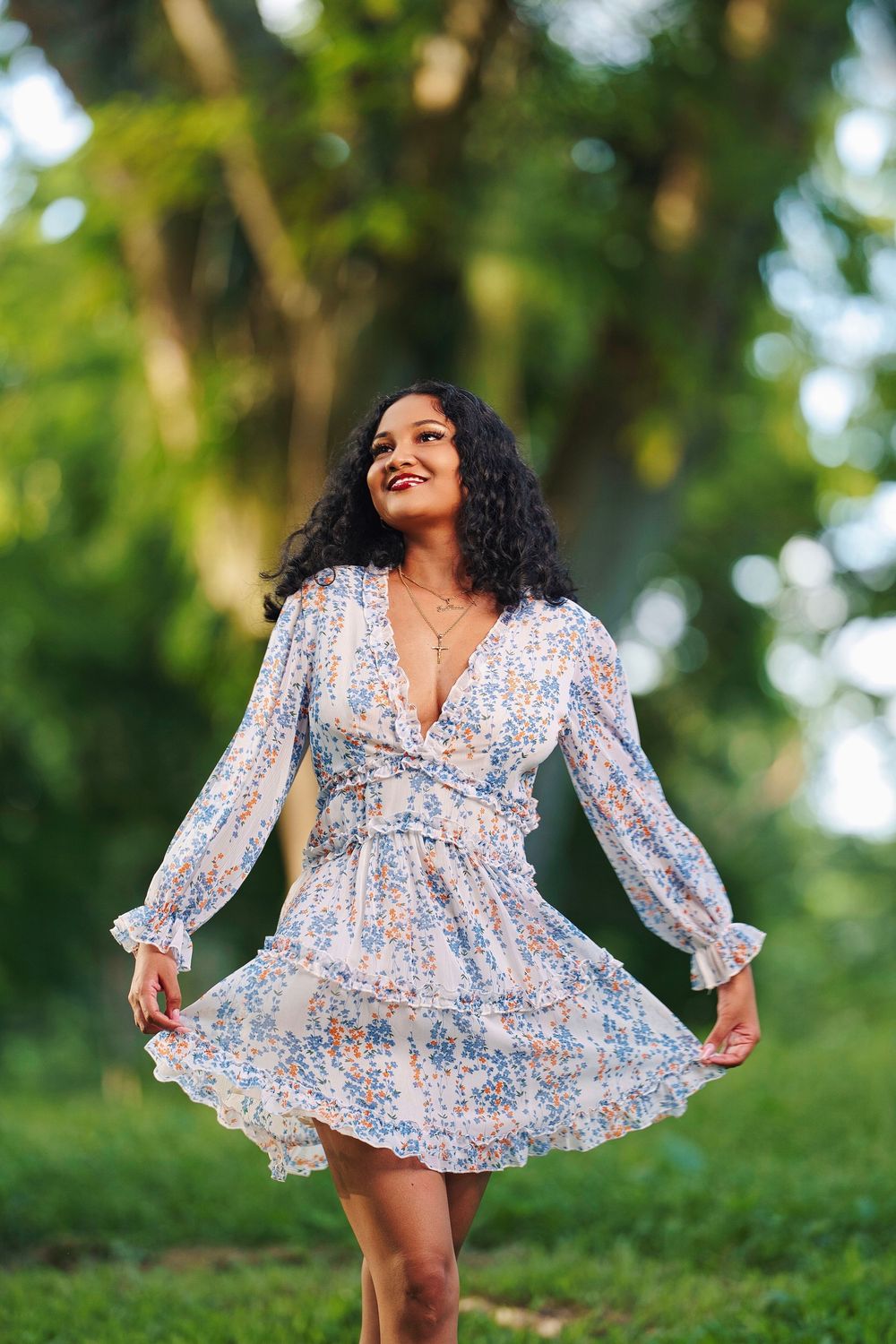 A flowing white and blue patterned dress shown in a playful outdoor photoshoot with natural forest backdrop.