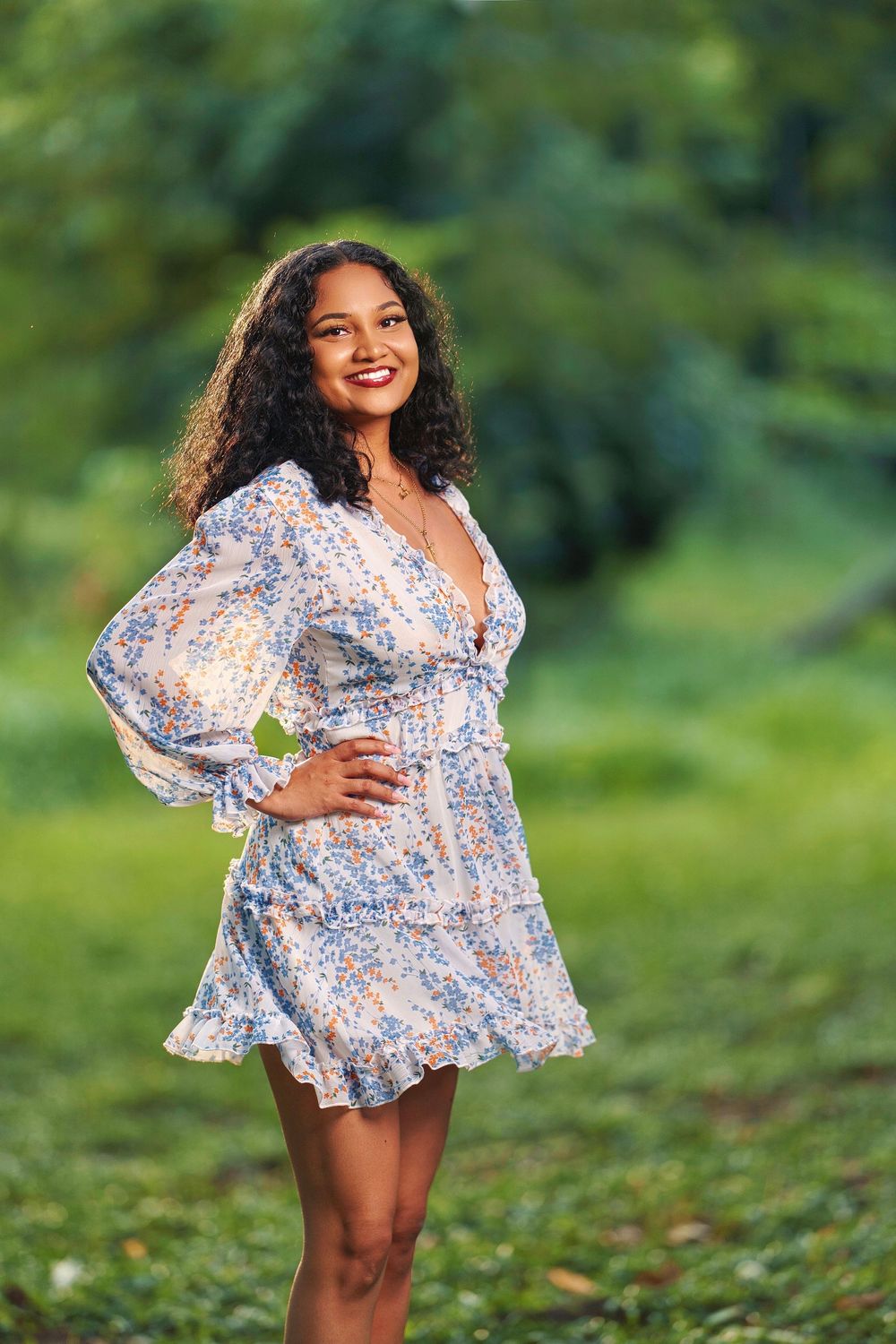 Woman in floral print mini dress with long sleeves poses outdoors in a natural setting with green foliage background.