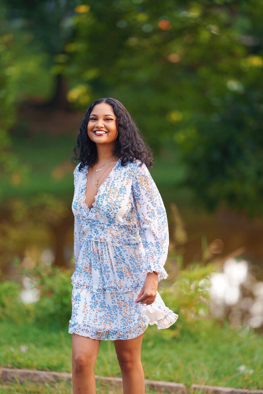 A person wearing a light blue floral print dress with long sleeves poses outdoors in a natural garden setting.