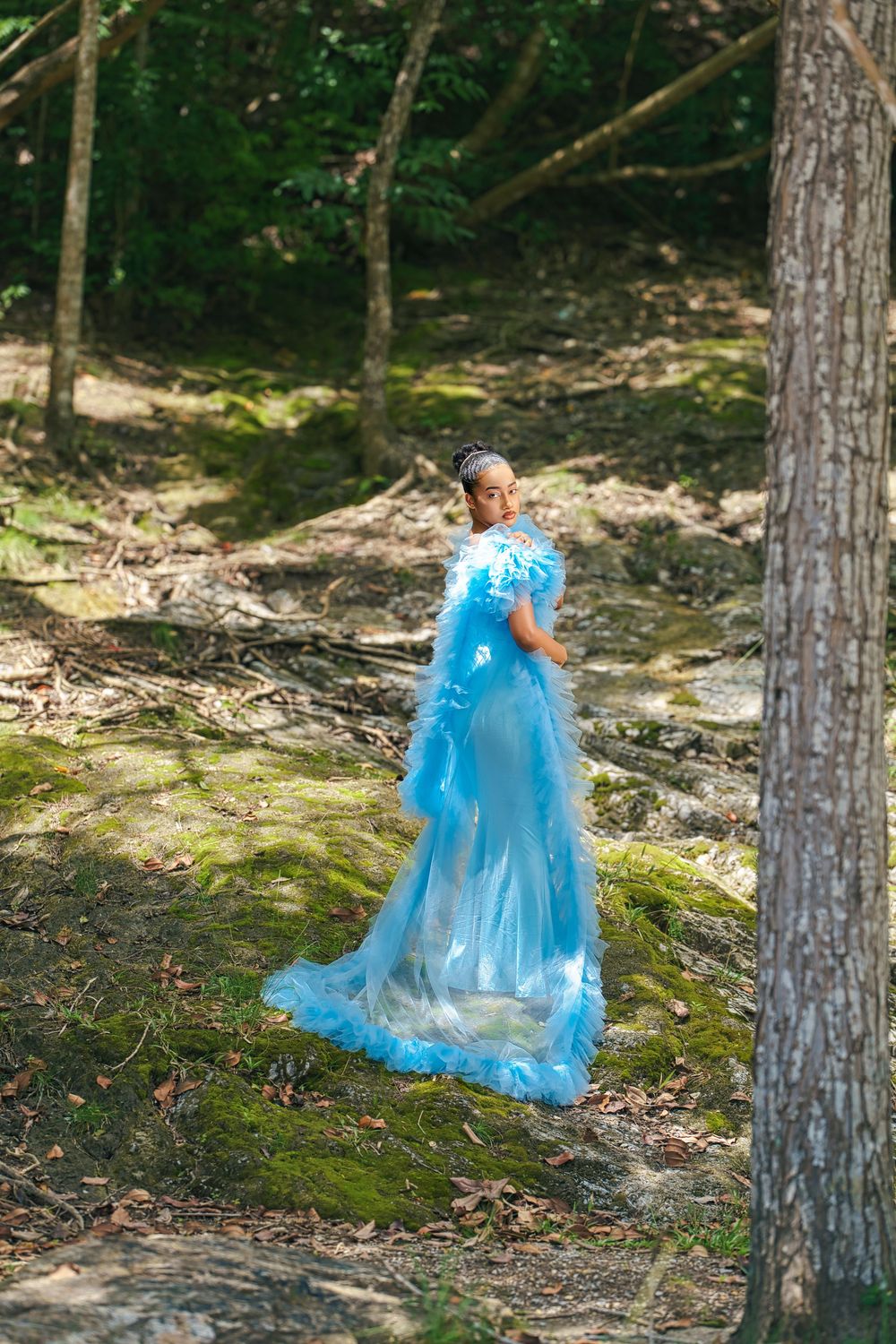 A series of dreamy maternity photos capturing movement in a light blue flowing dress among tall trees.