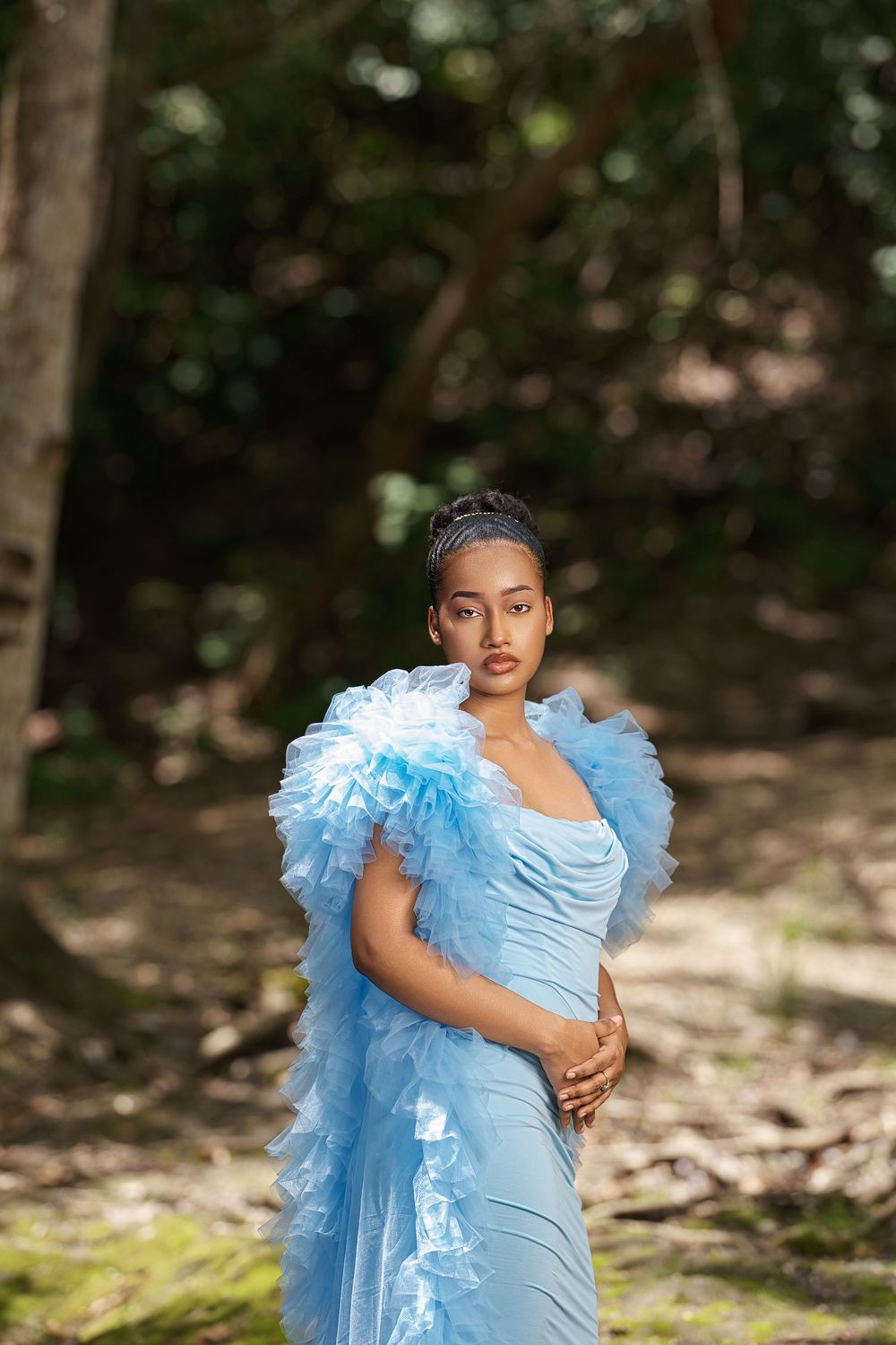 An ethereal maternity portrait featuring a powder blue gown with dramatic tulle sleeves in a forest setting.