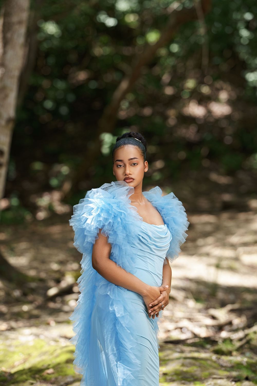 Ethereal outdoor photoshoot with flowing baby blue tulle gown in a sunlit woodland setting.