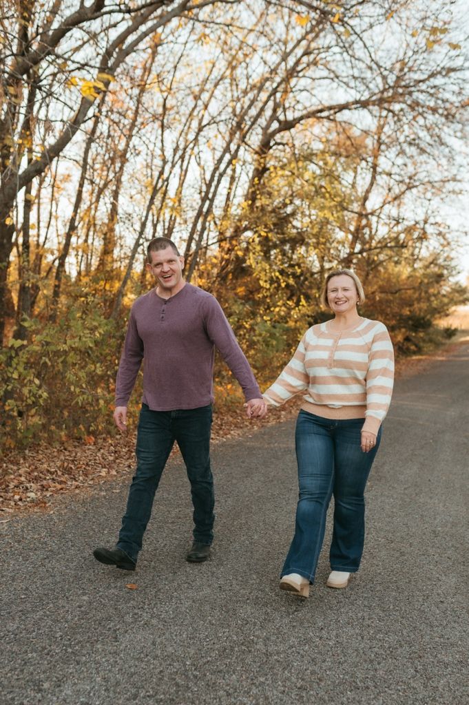 A couple walks together on a path surrounded by autumn trees with golden light filtering through the branches.