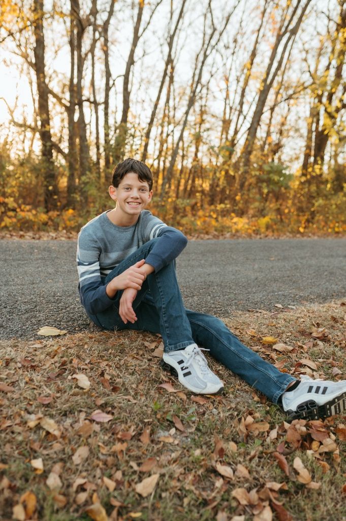 A person in casual attire lounges on autumn leaves during a fall photoshoot outdoors.