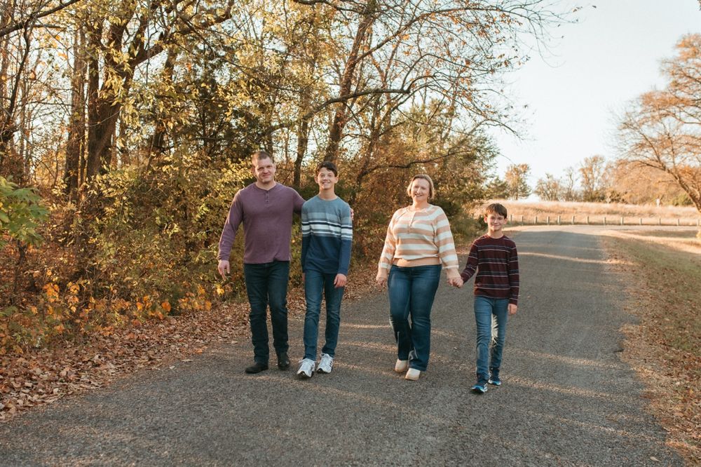 A group walks together on a paved path through autumn trees during golden hour.